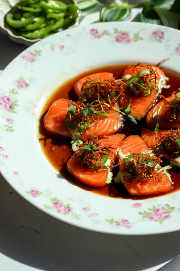Overhead view of salmon crudo with sweet ponzu sauce, creamy jalapeno sauce and crispy carrot matchsticks on a white plate.