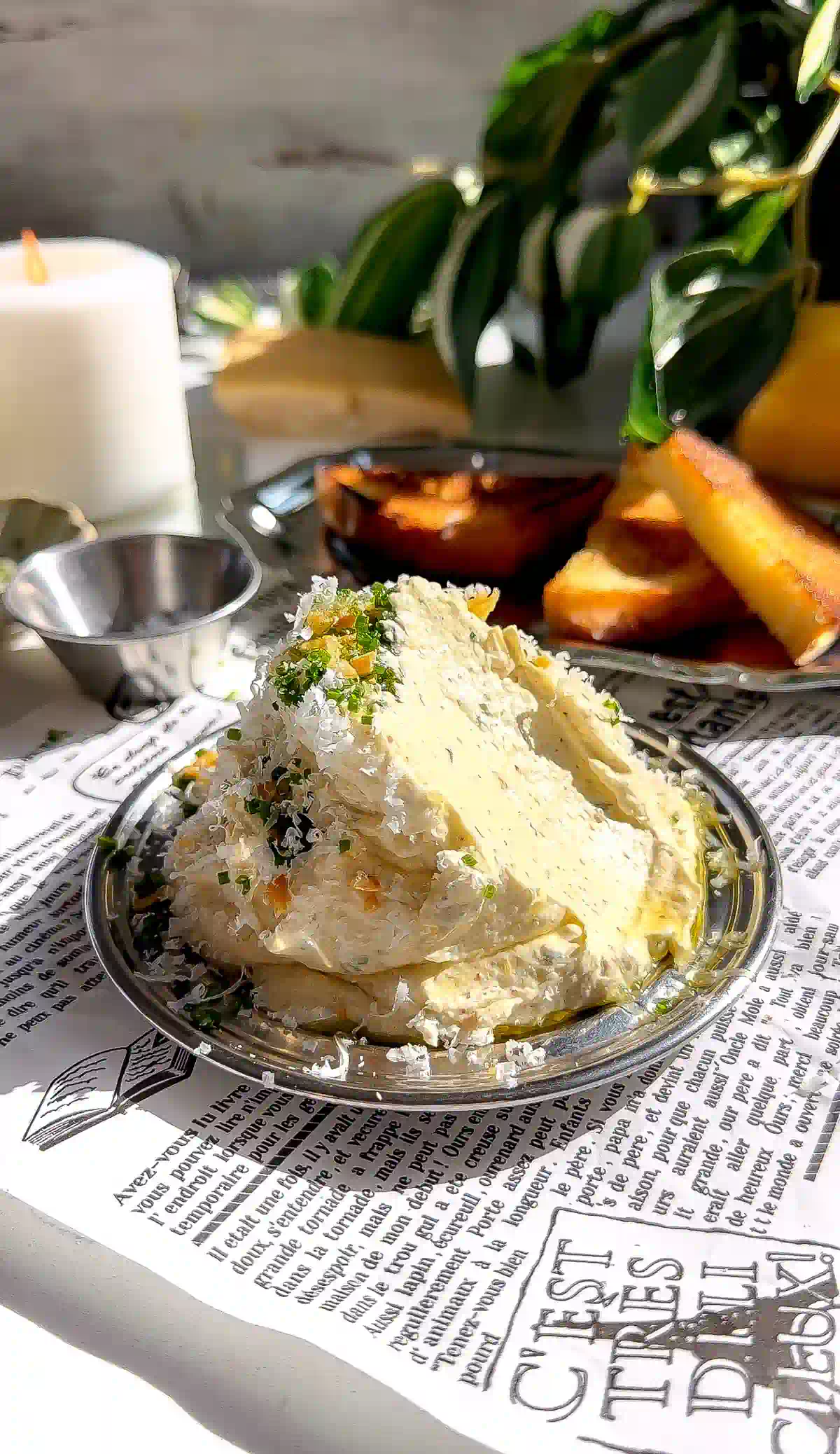 A silver dish of whipped roasted garlic butter with a scoop taken out, revealing the light, aerated texture of the spread, served over food-safe newsprint.