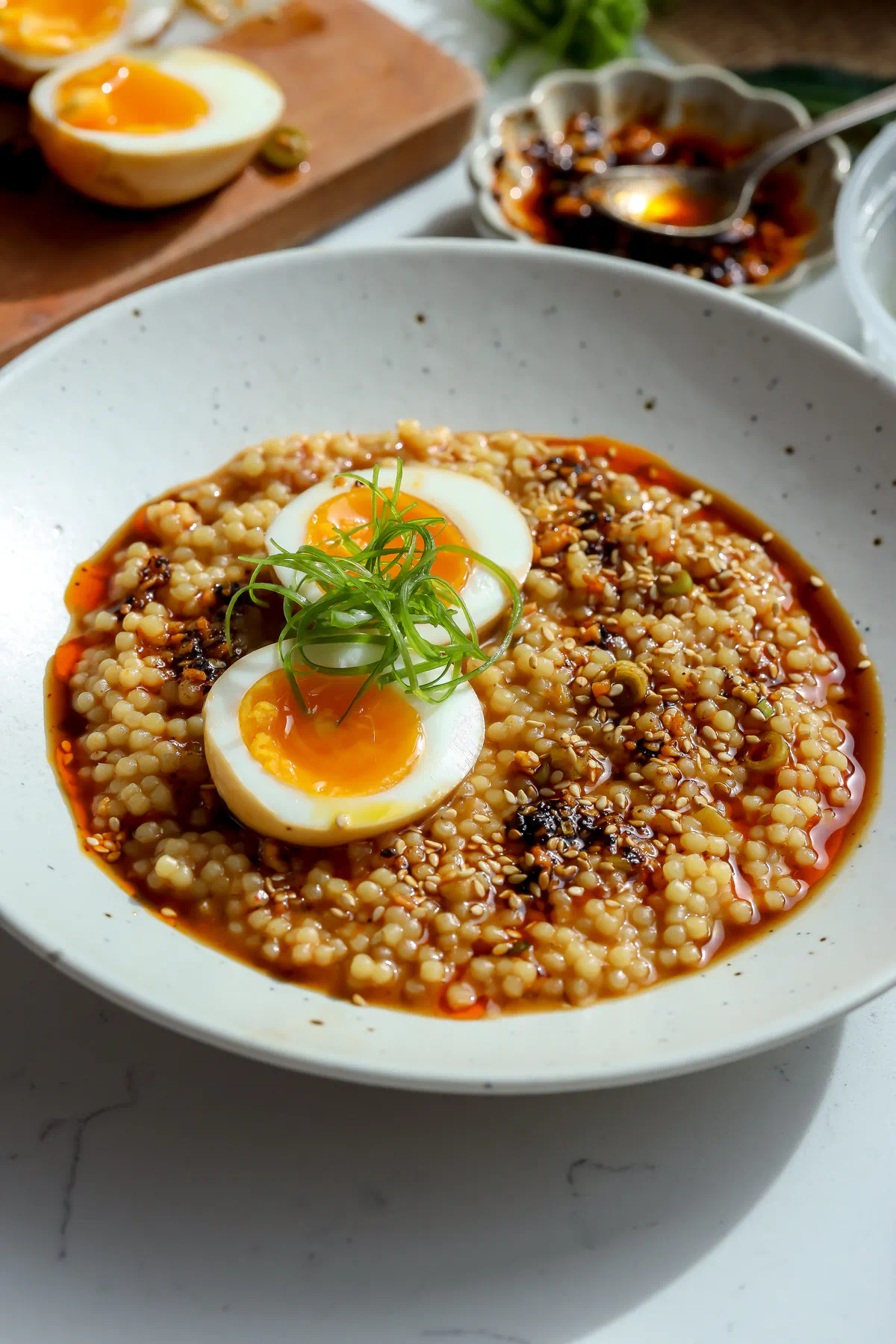 Creamy miso ramen pastina featuring tiny acini di pepe pasta, a halved jammy egg with a runny yolk, and vibrant green onion curls in a ceramic bowl.