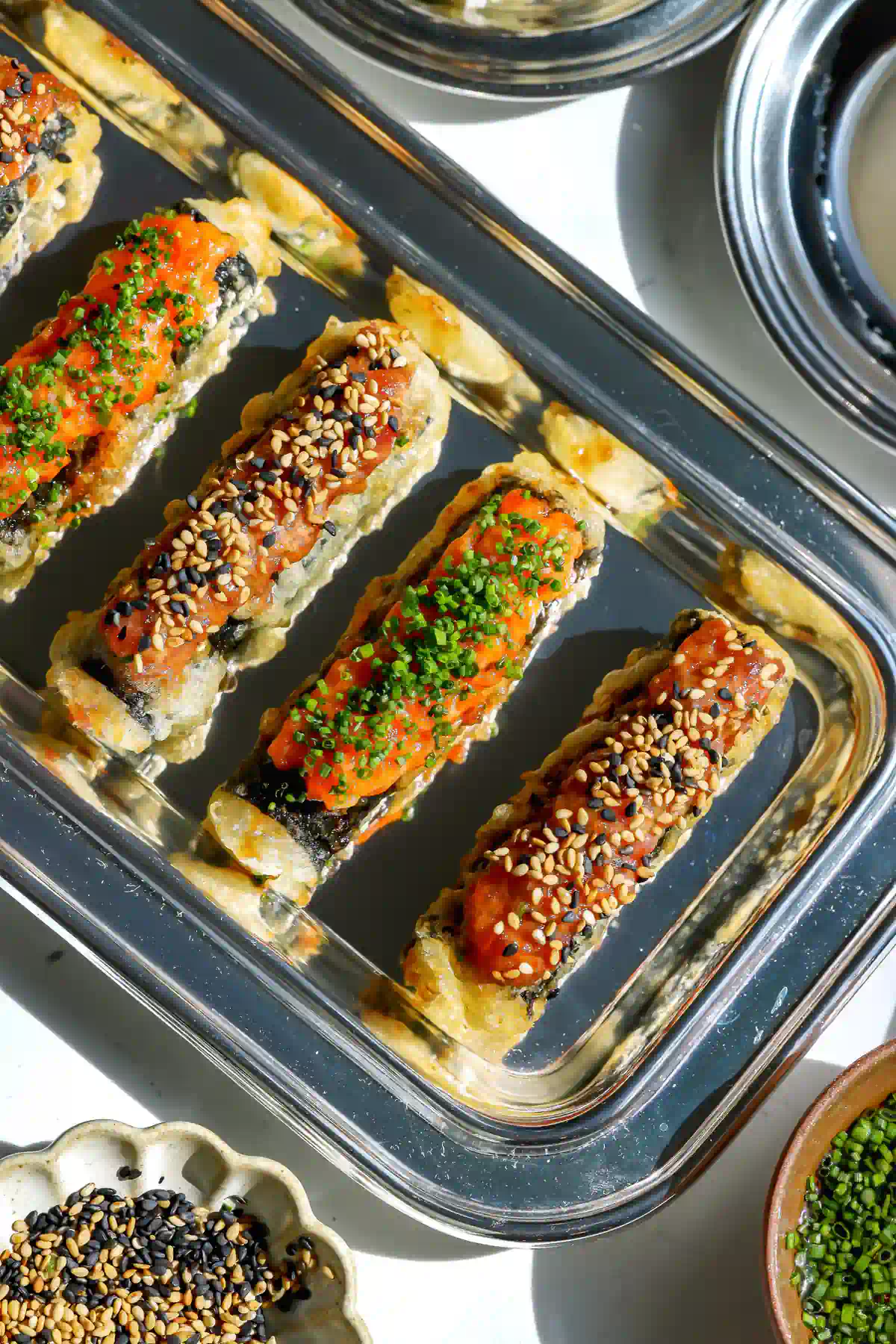 An overhead view of tempura sushi taquitos on a silver serving tray, topped with either creamy spicy tuna and sesame seeds or cured spicy salmon and fresh chives.