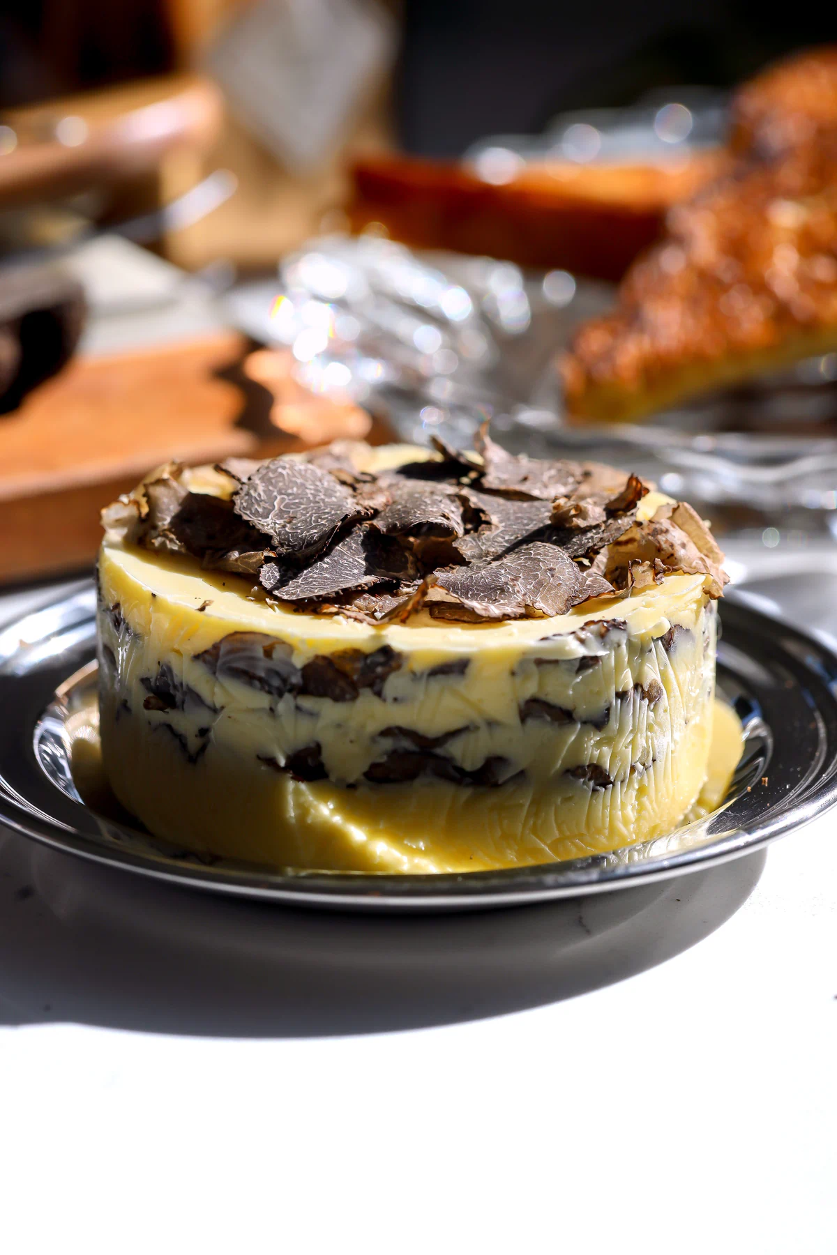 A thick disk of homemade compound truffle butter layered with shaved fresh black truffles resting on a silver plate.
