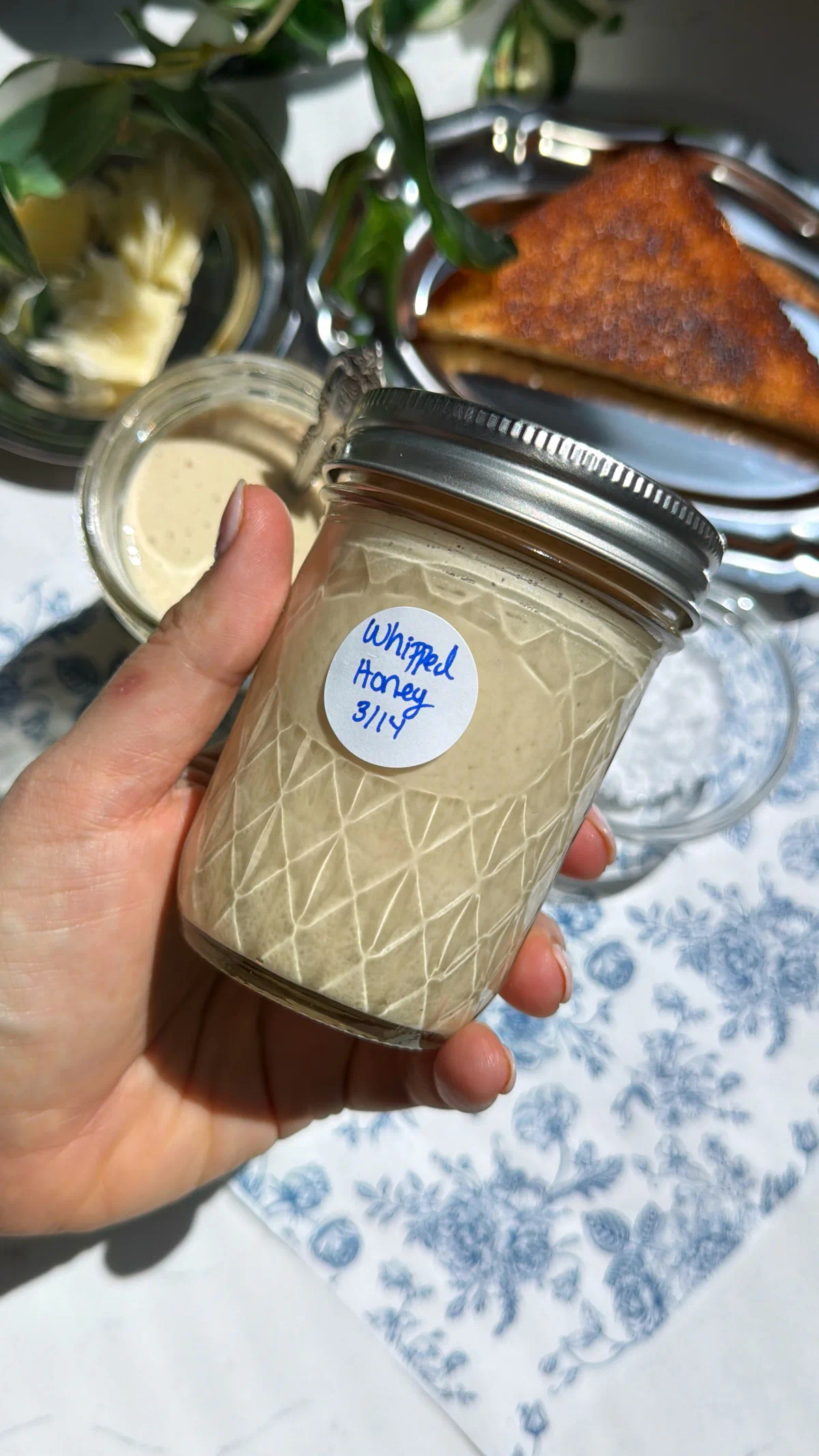 Creamy whipped honey in a jar being help up with a hand