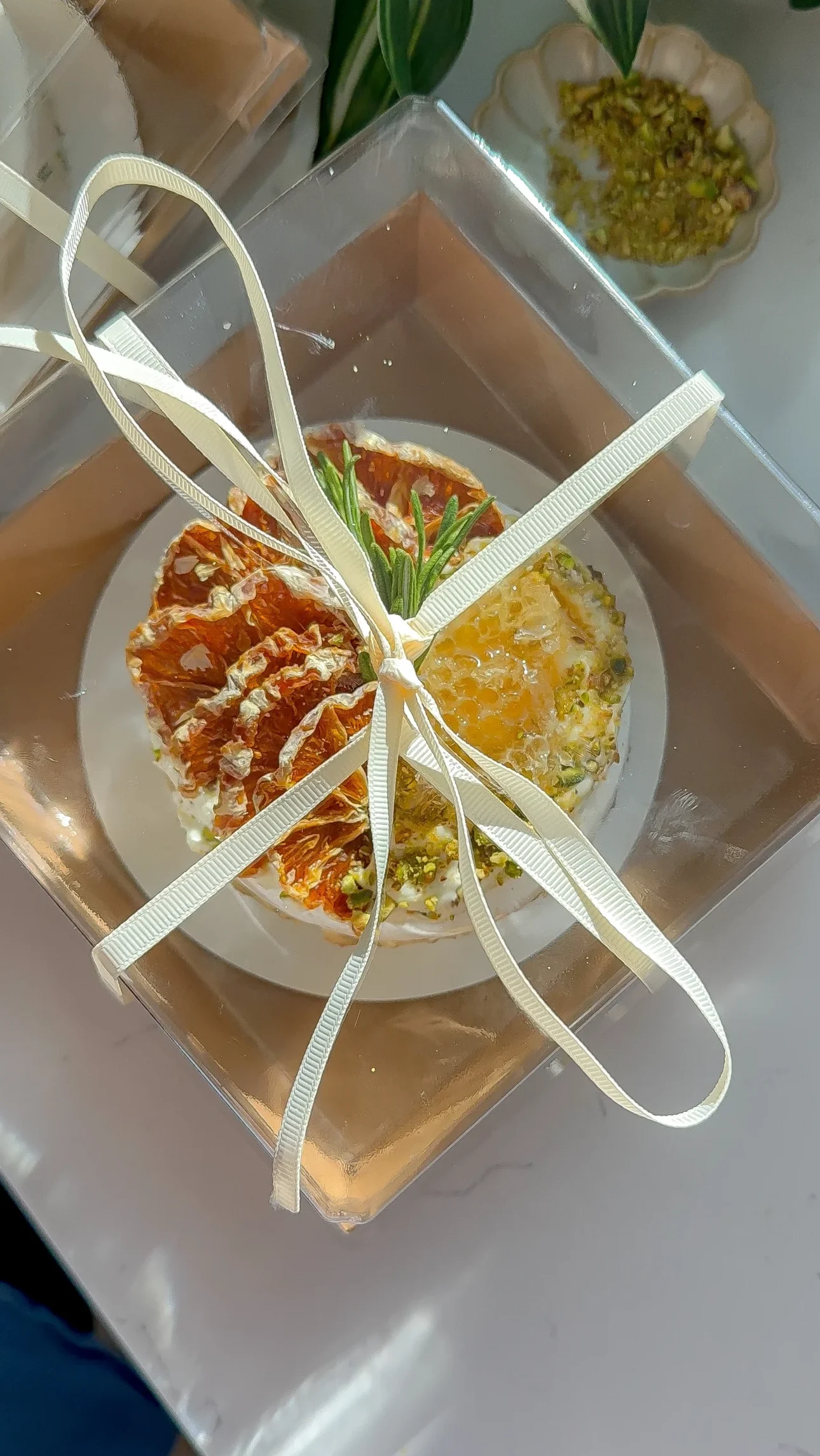 A top down view of a brie and fig appetizer wrapped in a clear gift box with ribbon and garnished with dried citrus and honeycomb.