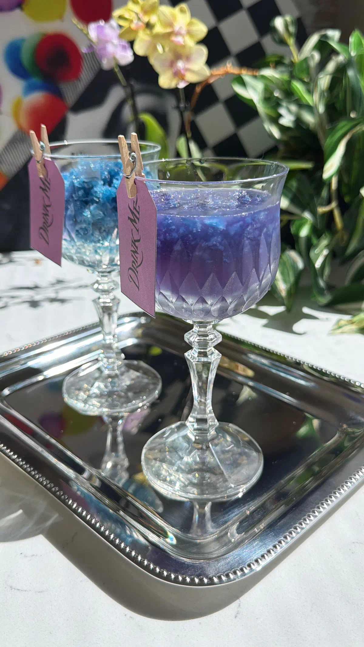 Two crystal glasses on a silver tray showing the galaxy cocktail color change. One glass contains just the blue butterfly pea granita, and the other shows the vivid purple mixed drink.