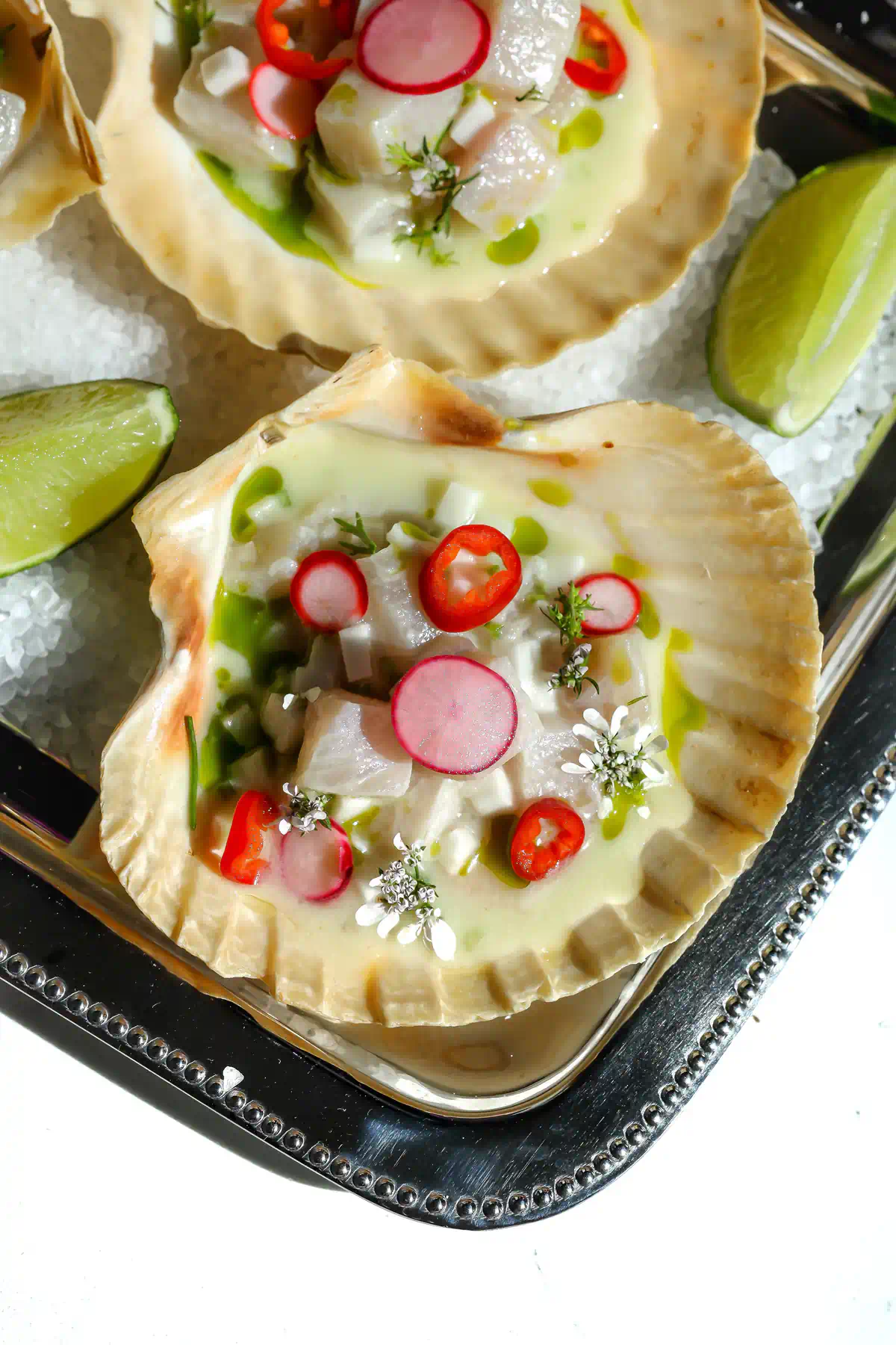 Overhead view of yellowtail ceviche in scallop shells topped with cilantro oil, pickled radish, and edible flowers.