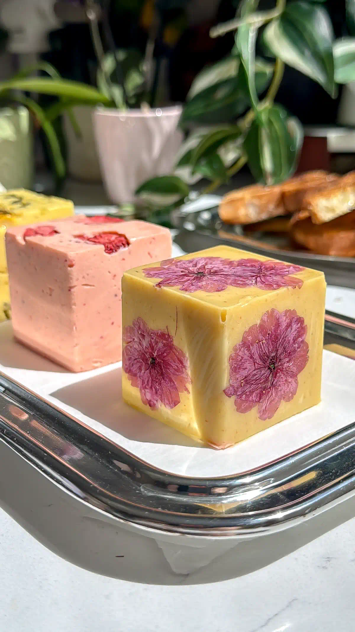 A square block of tahini maple compound butter pressed with pink cherry blossoms resting on a silver tray.