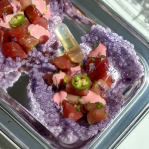 Overhead view of purple tapioca crisps filled with cured bluefin tuna, pink mayo, and a shiro dashi ponzu syringe on a silver platter.