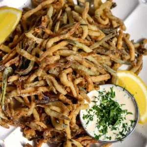 Overhead view of deep fried zucchini and eggplant fries on a white scalloped plate with creamy garlic herb dipping sauce and lemon wedges.