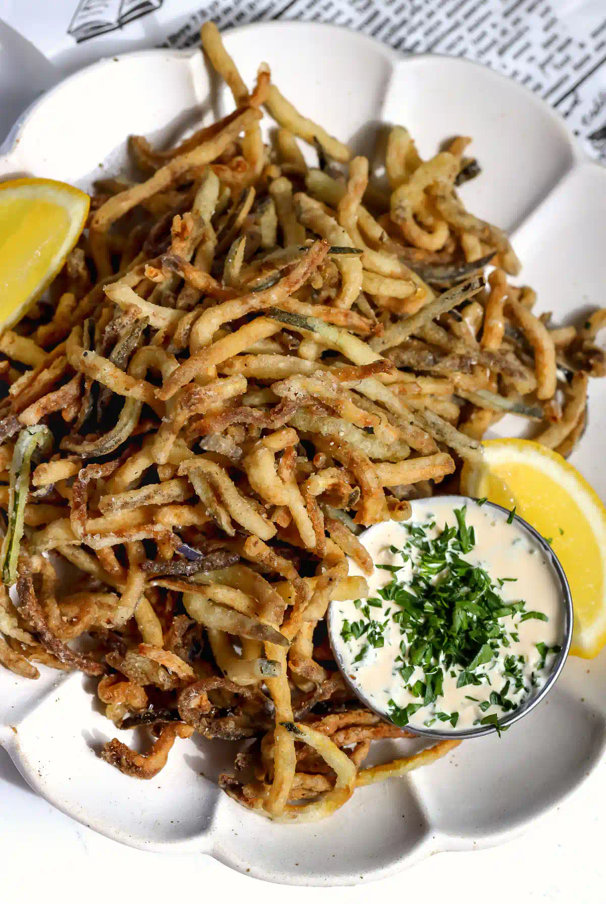 Overhead view of deep fried zucchini and eggplant fries on a white scalloped plate with creamy garlic herb dipping sauce and lemon wedges.
