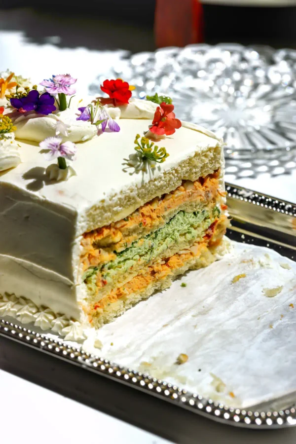 Sliced Sandwichon showing alternating layers of chipotle chicken salad and herb cheese spread between brioche bread on a silver platter.