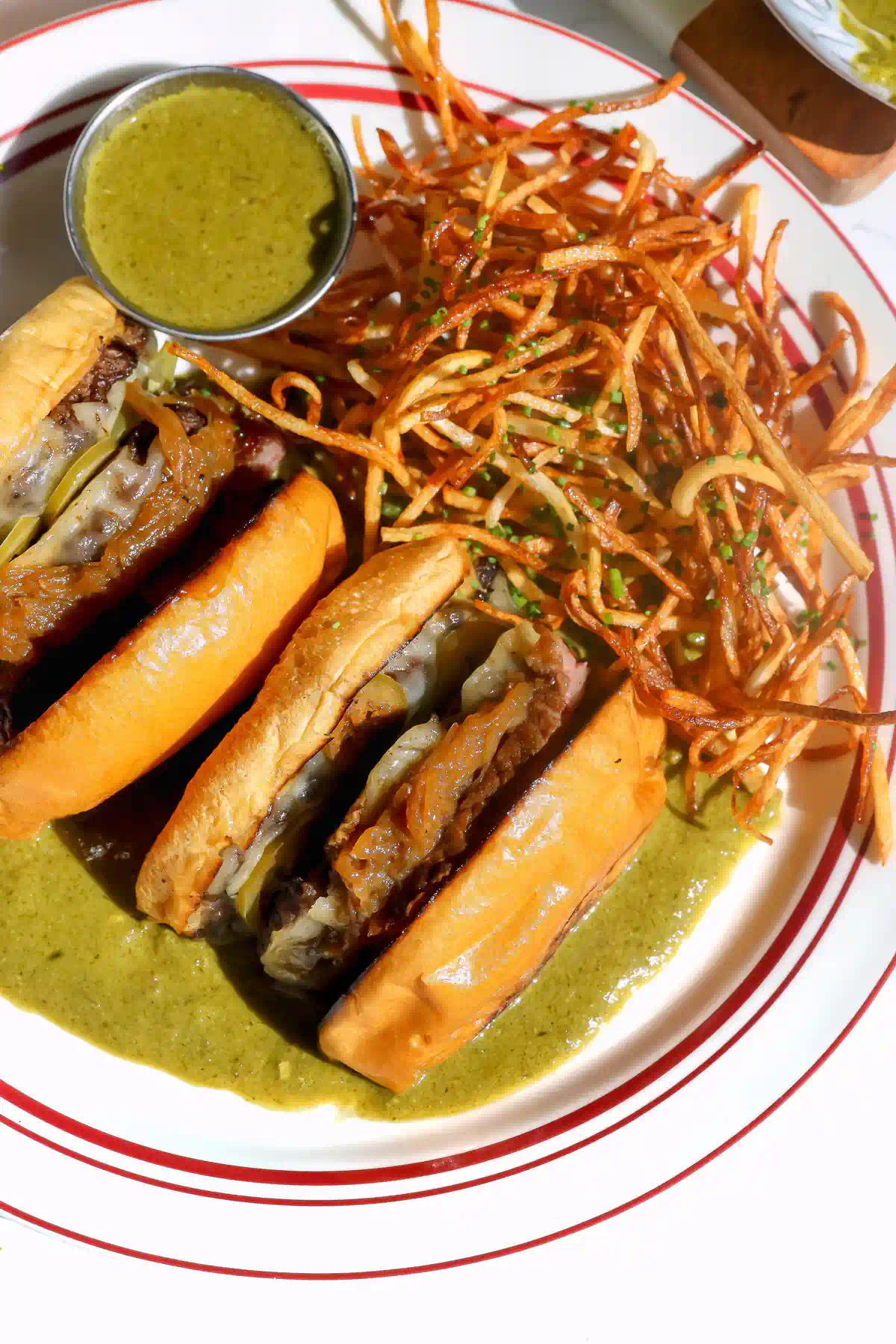 Overhead of a wagyu burger cut in half in green entrecôte sauce with matchstick frites and a ramekin of extra sauce