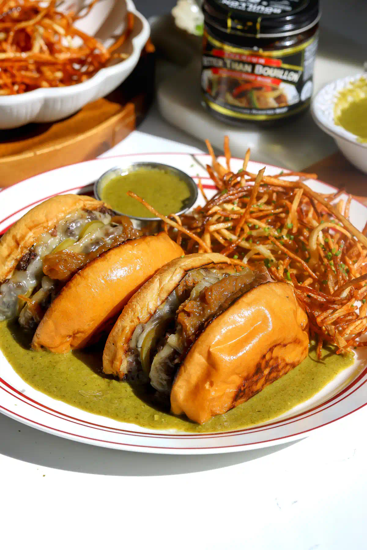 Wagyu burger halves in green entrec&ocirc;te sauce with a ramekin of sauce and matchstick frites, a jar of Better Than Bouillon behind