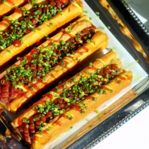 Overhead view of crescent roll hot dogs showing the crosshatch scored hot dogs in golden crescent dough, drizzled with spicy ketchup and mustard mayo.