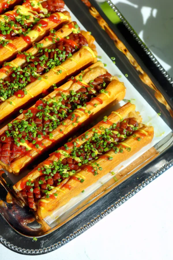 Overhead view of crescent roll hot dogs showing the crosshatch scored hot dogs in golden crescent dough, drizzled with spicy ketchup and mustard mayo.