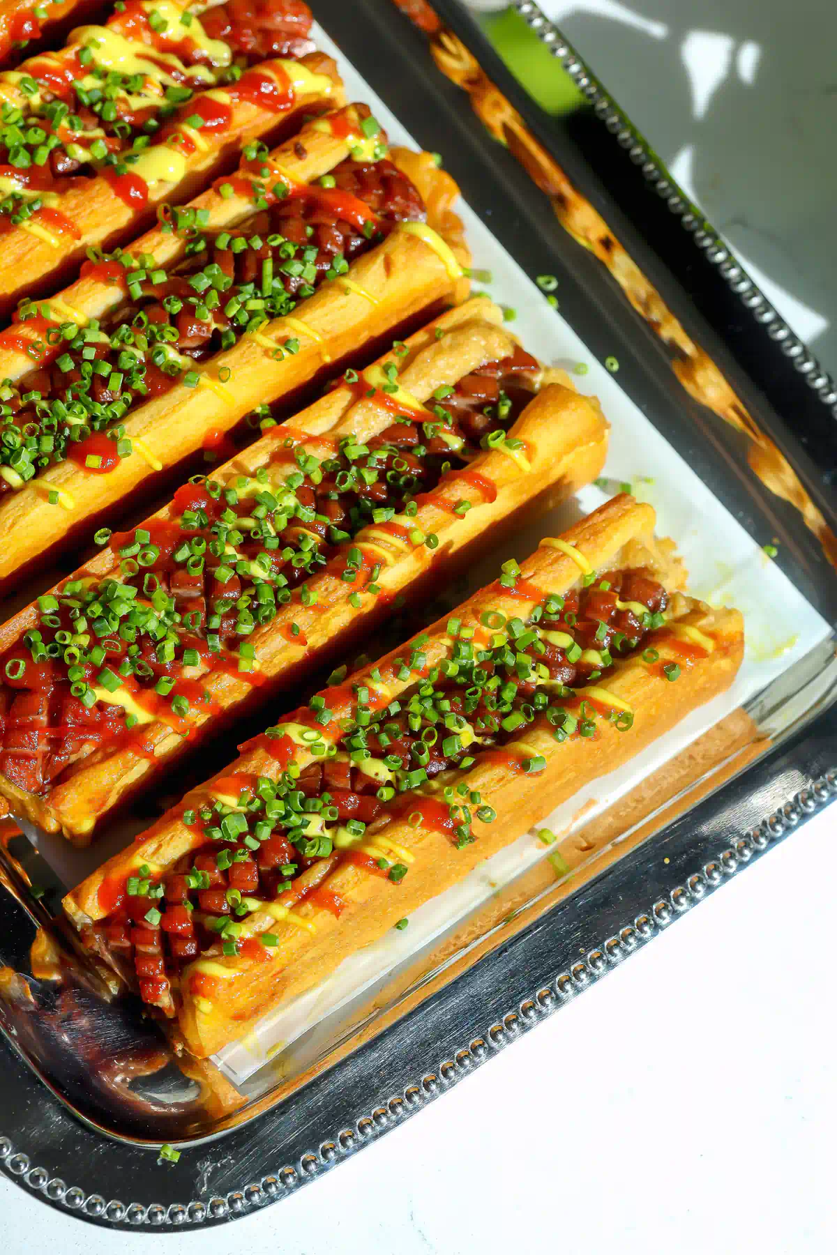 Overhead view of crescent roll hot dogs showing the crosshatch scored hot dogs in golden crescent dough, drizzled with spicy ketchup and mustard mayo.