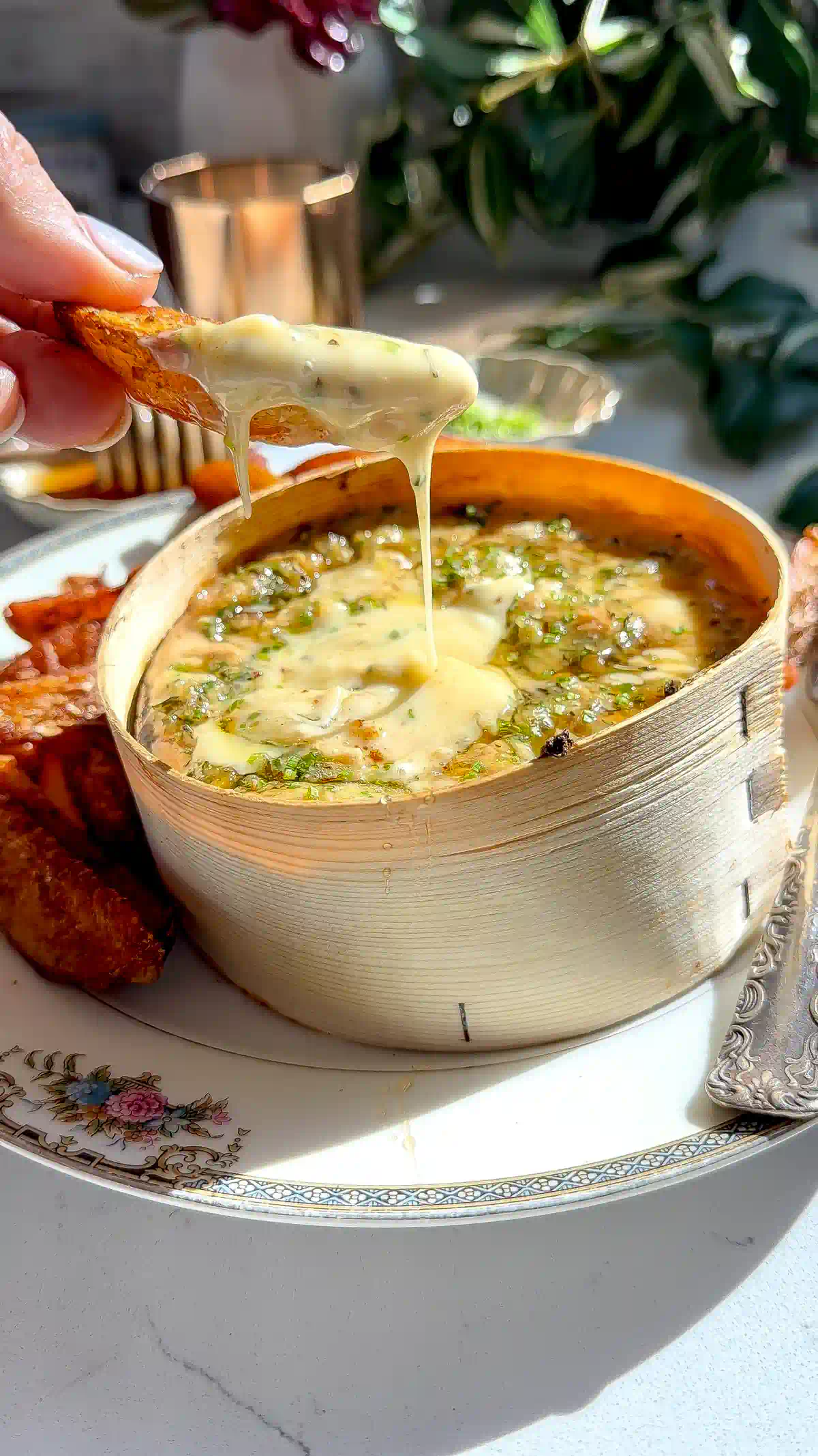 A crispy roasted potato lifting a string of melted cheese from a box of baked Mont d'Or.