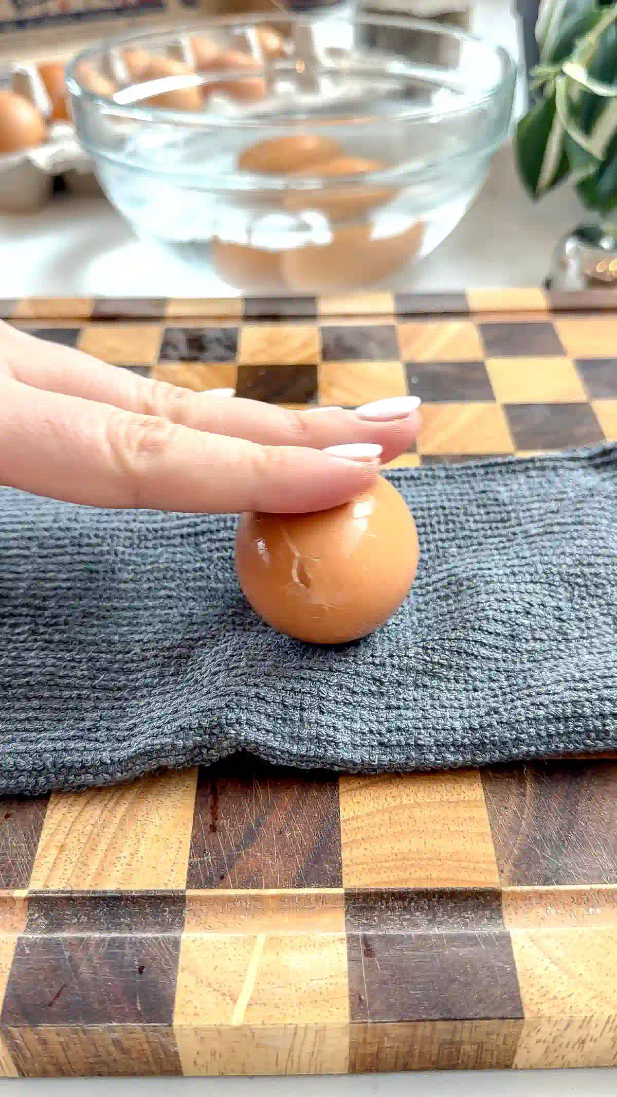 A hand pressing a boiled egg on a towel to crack the shell