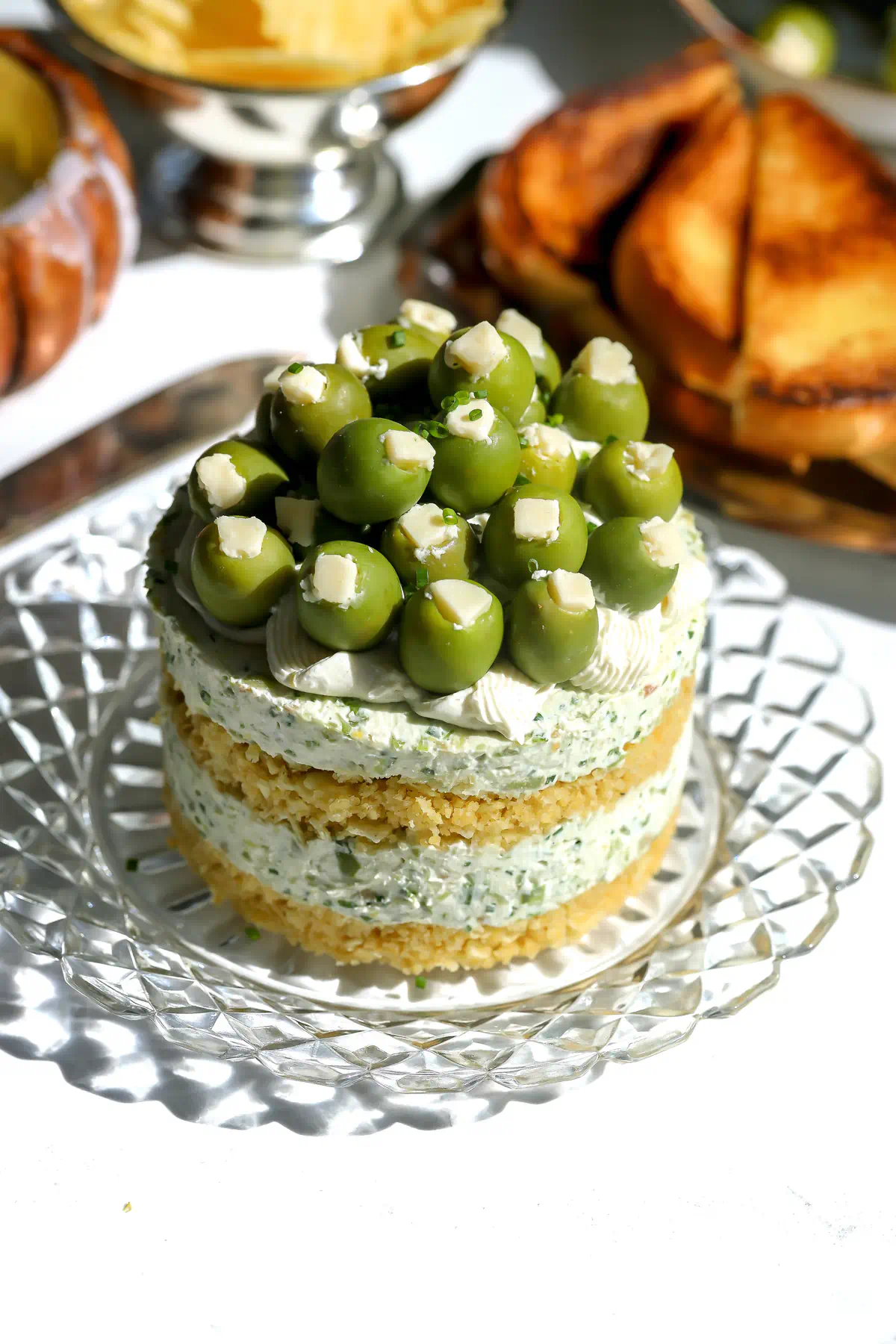 Top of a dirty martini cheesecake covered in castelvetrano olives, blue cheese pieces, and chives over piped cream cheese.