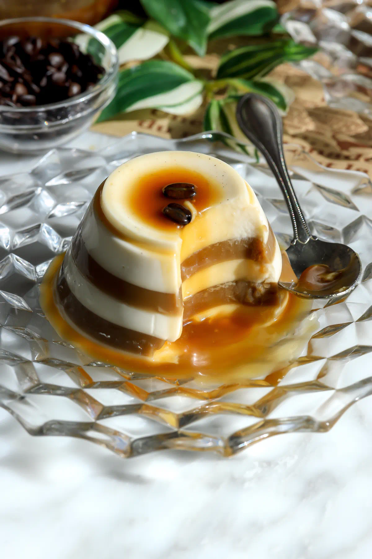 An espresso eggnog panna cotta with a spoonful taken out, showing the espresso and eggnog stripes inside and caramel pooled on the plate.