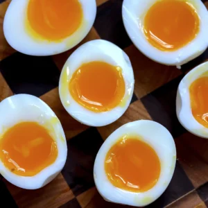 Six soft boiled egg halves on a wooden board with set whites and jammy yolks
