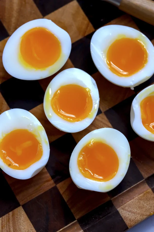 Six soft boiled egg halves on a wooden board with set whites and jammy yolks