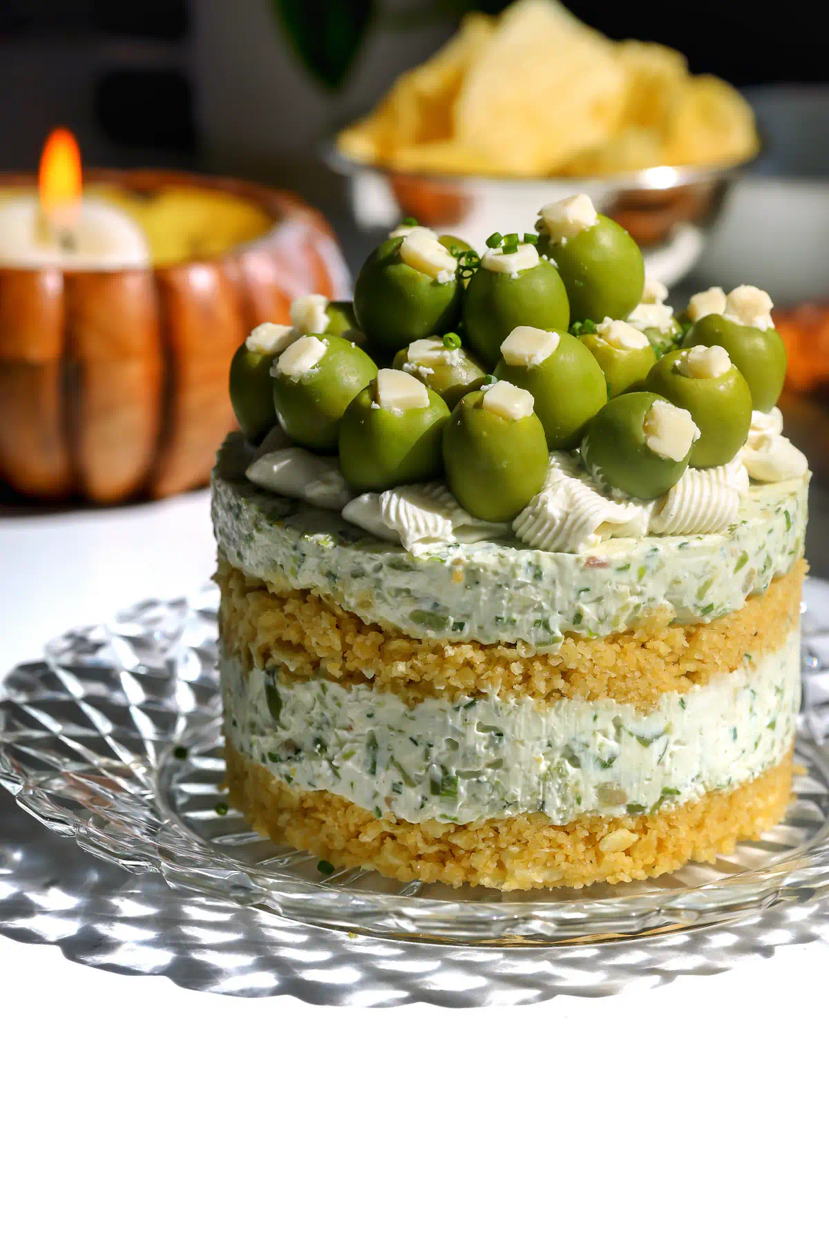 A whole savory dirty martini cheesecake with ritz and potato chip crust layers, blue cheese cream filling, and green olives on top.