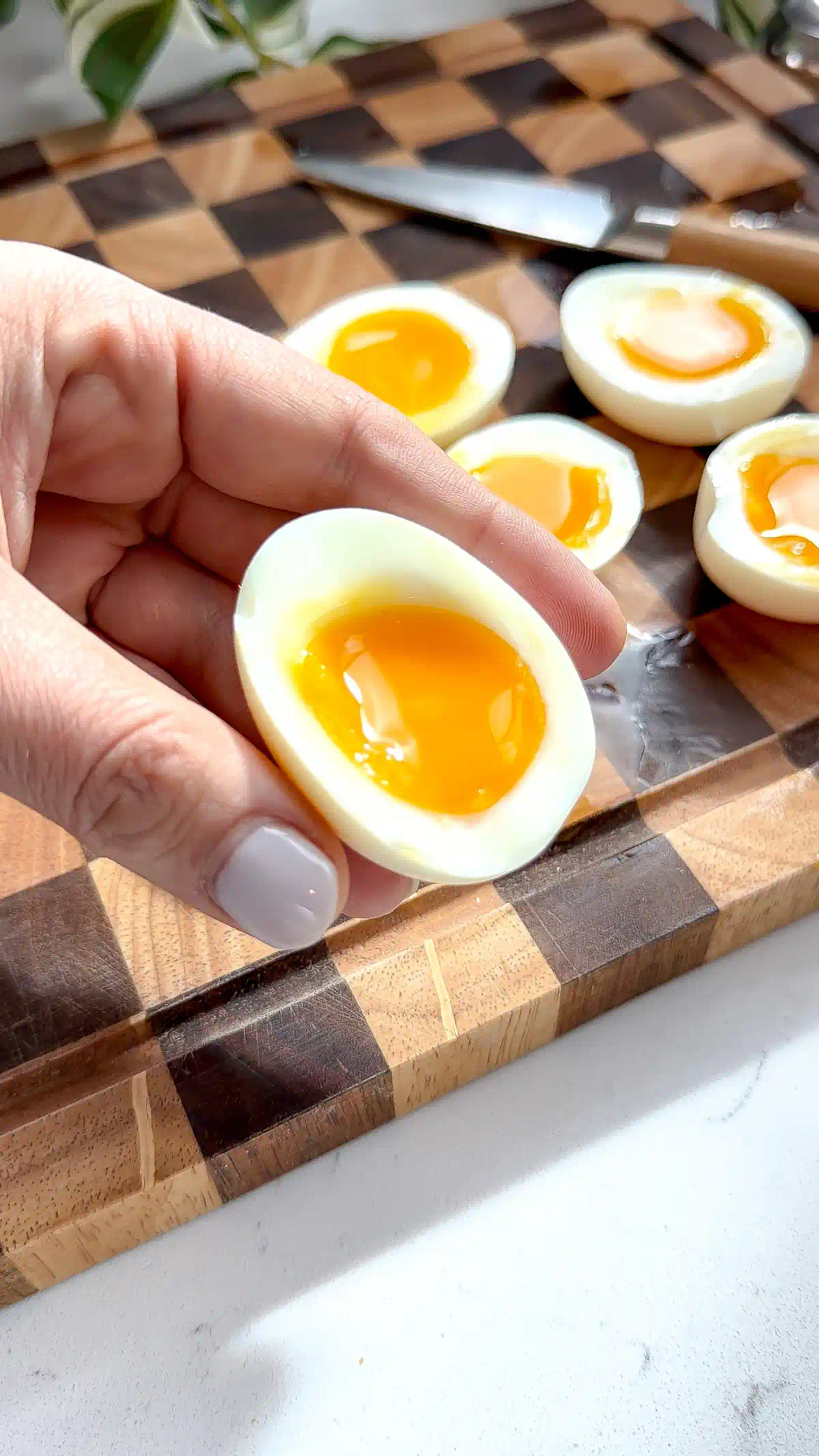 A hand holding a soft boiled egg half with a jammy center