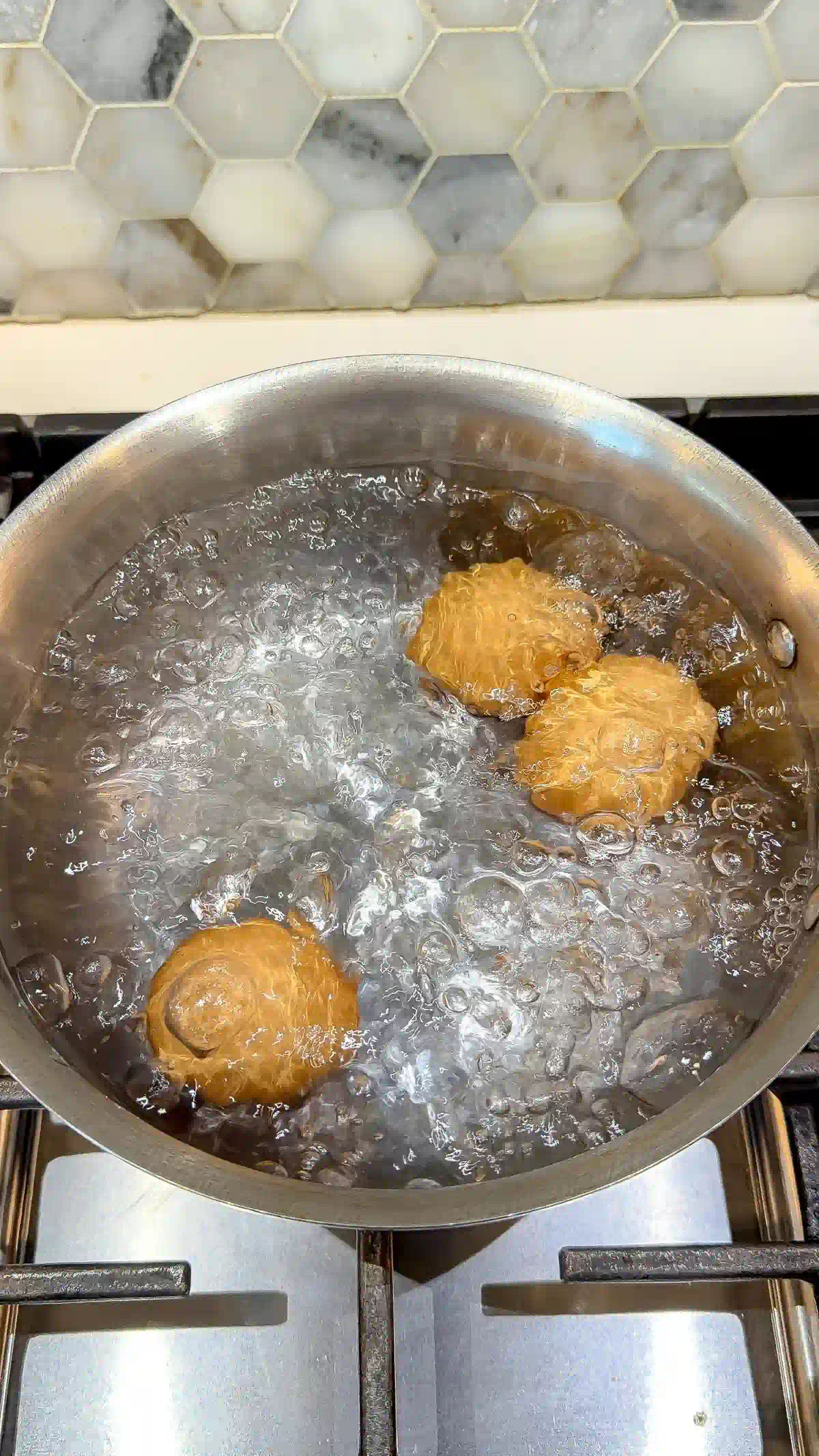 Three brown eggs in a pot of rapidly boiling water
