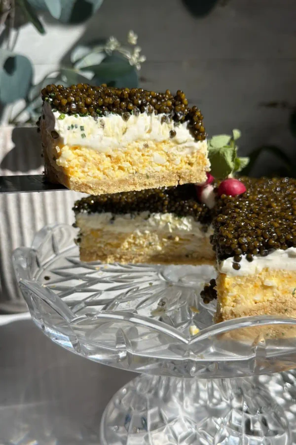 A slice of caviar pie lifted from the stand, showing the ritz crust, egg mousse, crème fraîche, and caviar layers.