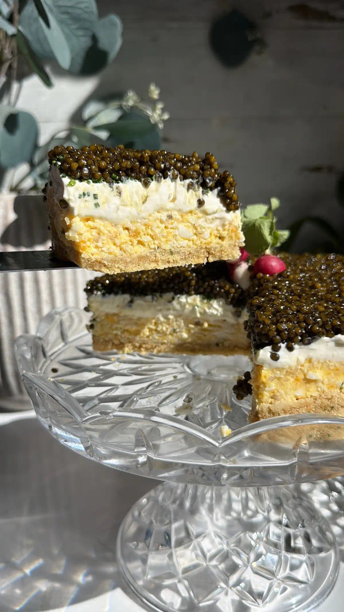 A slice of caviar pie lifted from the stand, showing the ritz crust, egg mousse, crème fraîche, and caviar layers.