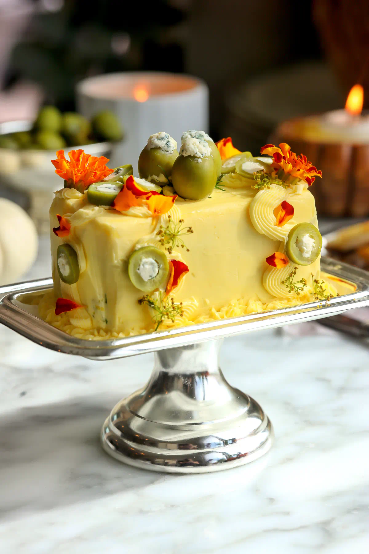 The side of a dirty martini butter cake decorated with sliced stuffed olives, piped swirls, orange edible flowers, and dill flowers