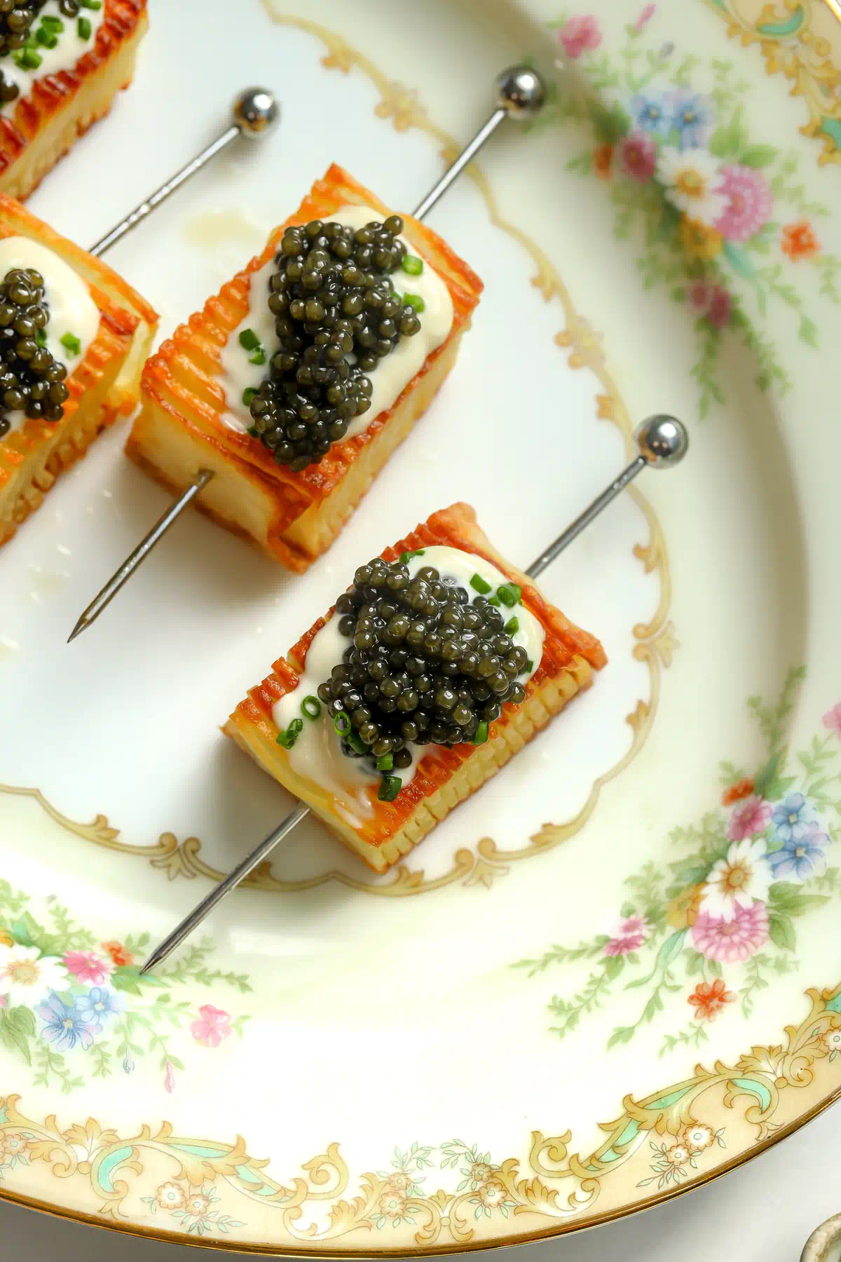 Overhead view of potato stacks on silver cocktail picks, each topped with a mound of caviar over crème fraîche and chives.