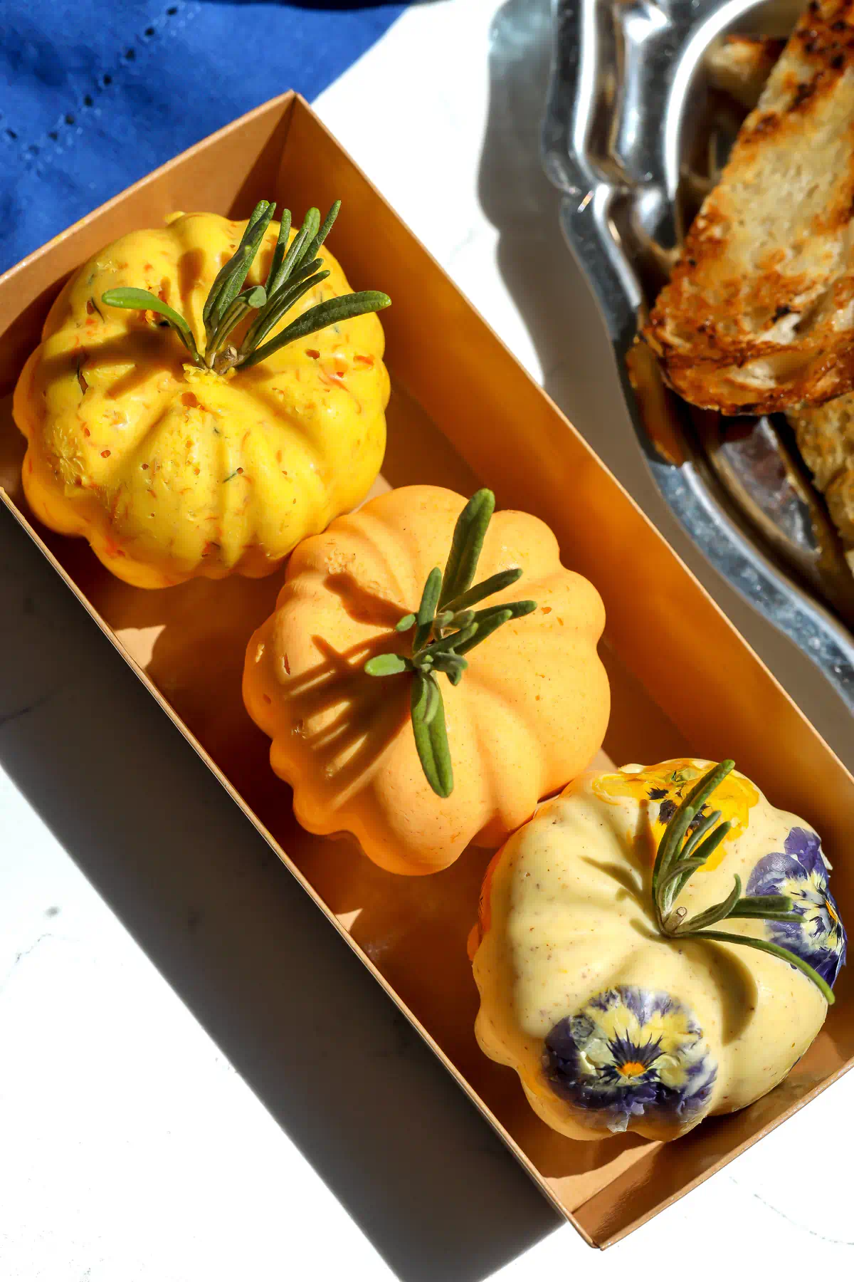 Overhead view of three butter pumpkins nestled in a rectangular gift box, decorated with rosemary stems and edible flowers.