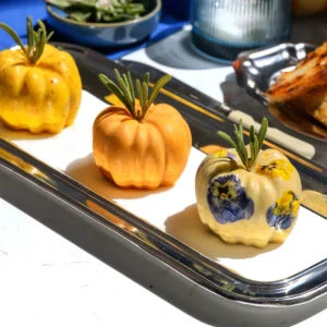 Roasted garlic pumpkin, pumpkin cinnamon roll, and maple pecan brown butter pumpkins lined up on a silver serving tray.