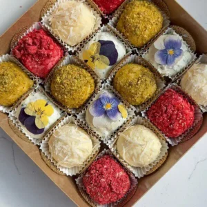 Cheese truffles coated in pistachios, raspberries, and parmesan or topped with edible flowers, arranged in a gift box.