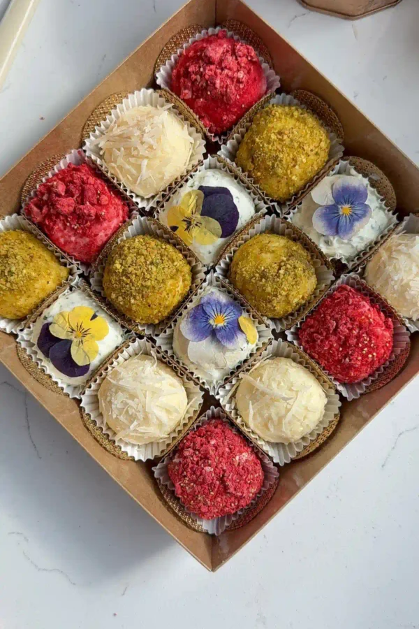 Cheese truffles coated in pistachios, raspberries, and parmesan or topped with edible flowers, arranged in a gift box.