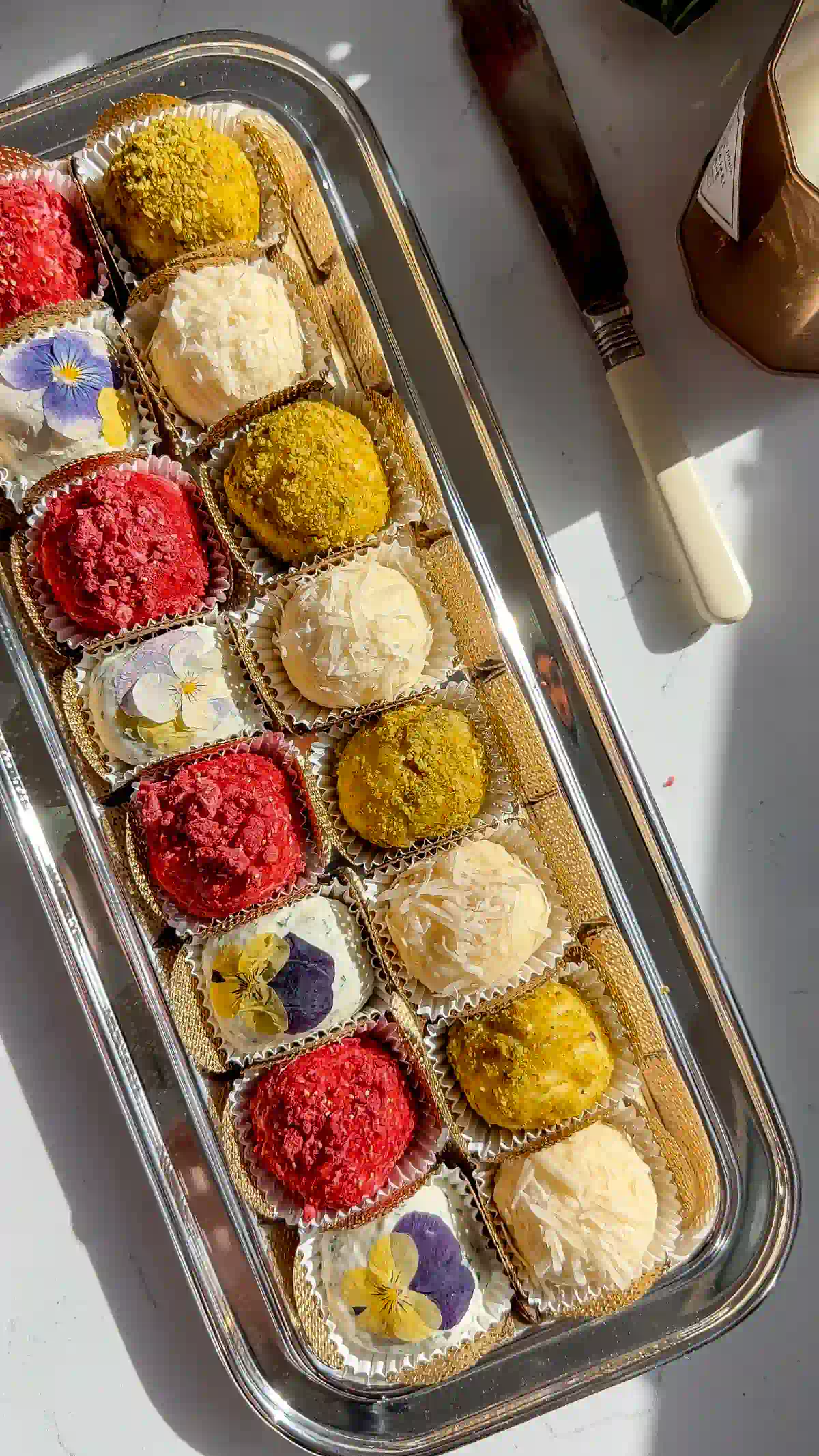 Four varieties of cheese truffles in white liners and gold fabric cups on a silver serving tray.