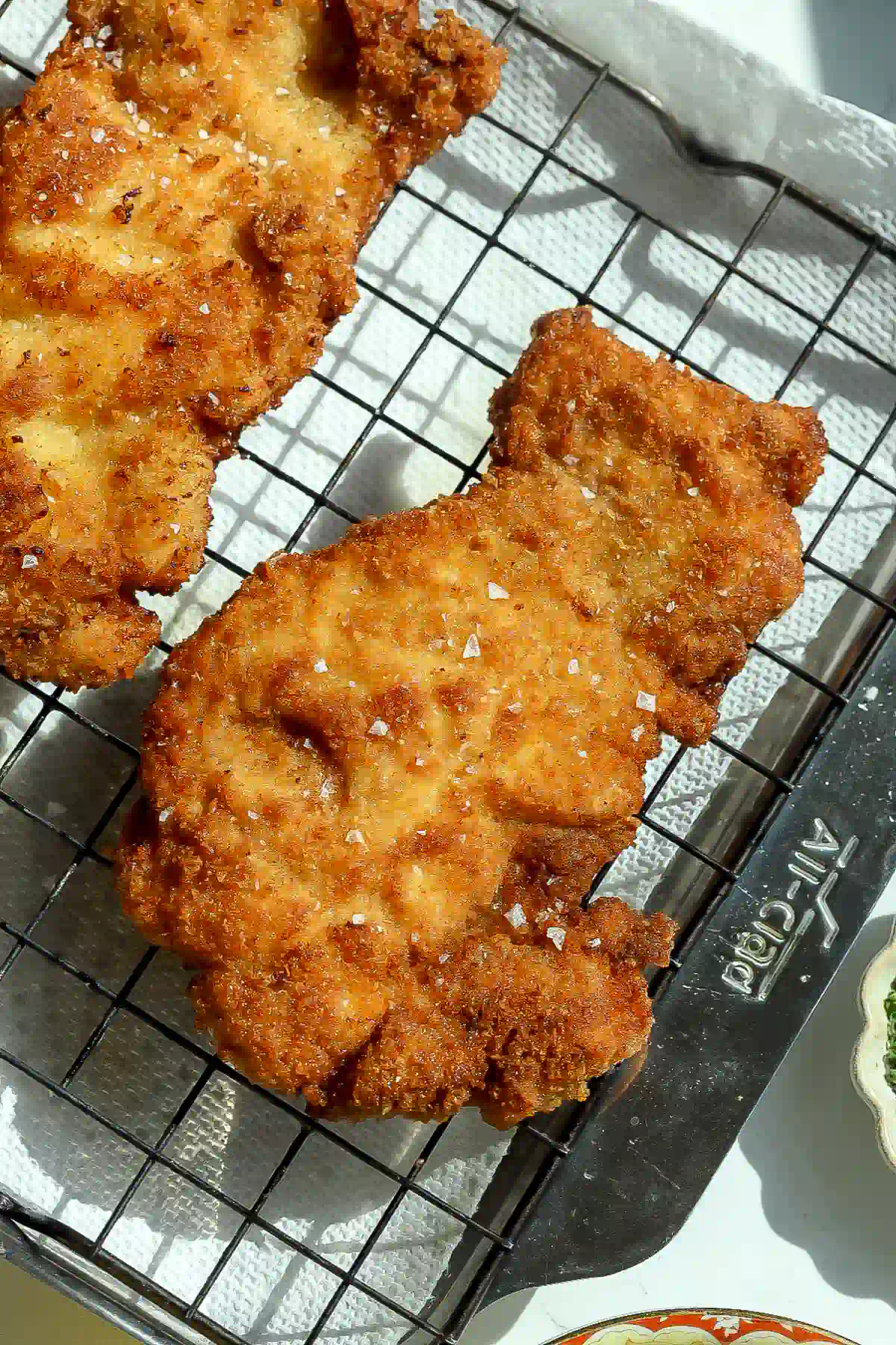 Golden panko-crusted chicken thighs sprinkled with flaky salt, resting on a wire rack over a sheet pan.
