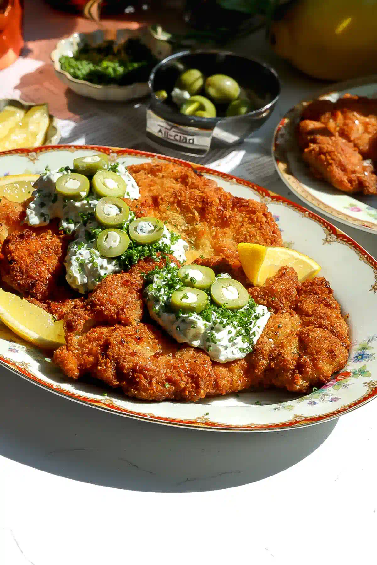 Angled view of crispy chicken topped with olive and blue cheese tartar sauce, sliced stuffed olives and chopped chives.