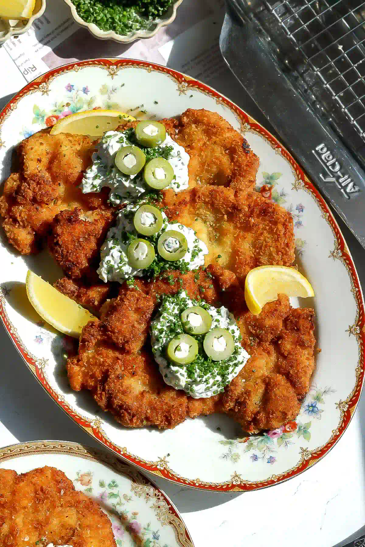 Overhead view of dirty martini chicken topped with tartar sauce, blue cheese stuffed olives and chives, with lemon wedges.