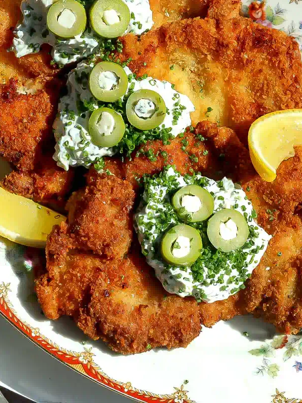 Crispy dirty martini chicken on a floral platter with creamy tartar sauce, blue cheese stuffed green olives and lemon wedges.