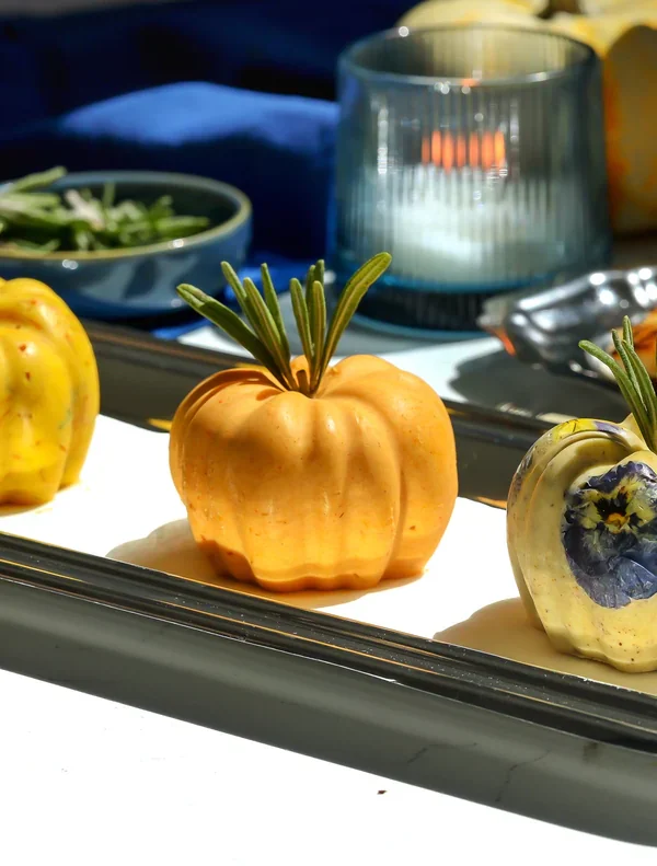 Three butter pumpkins topped with rosemary sprigs on a silver platter beside toasted bread and a lit candle.