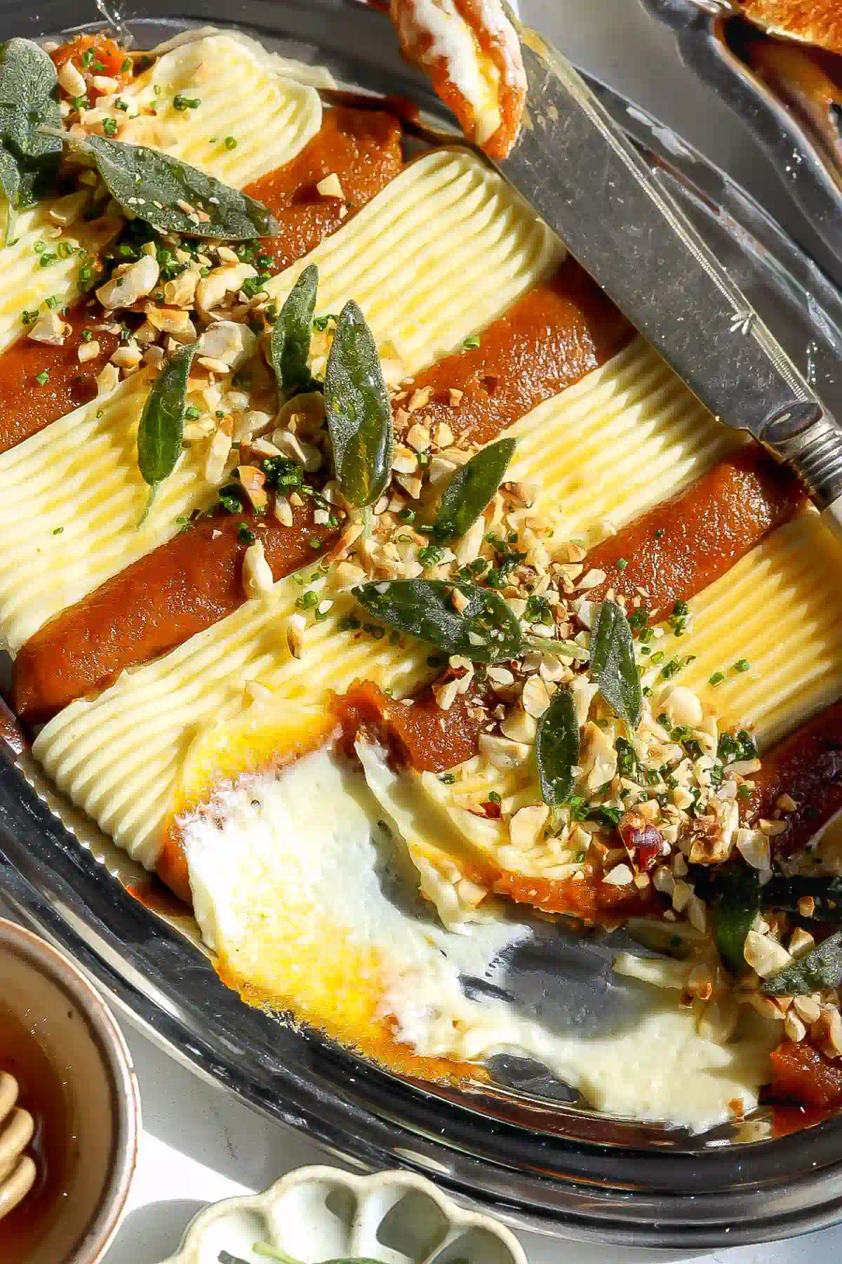 Pumpkin butter and whipped brie dip with a portion scooped out, showing the creamy texture beneath fried sage and hazelnuts.