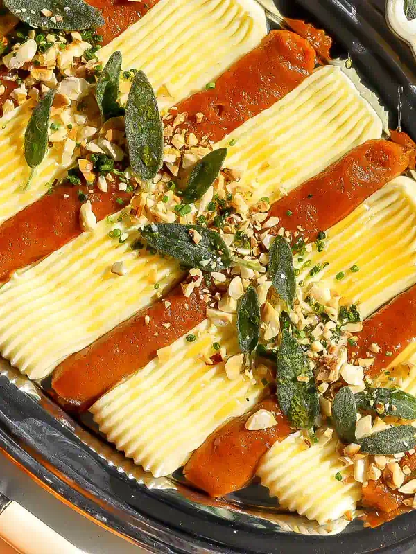 Overhead view of alternating strips of pumpkin butter and whipped brie topped with fried sage, chopped hazelnuts, and chives.