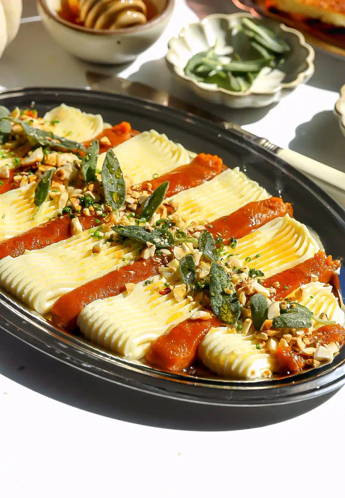 Piped whipped brie and pumpkin butter arranged in rows on a silver platter, finished with sage, hazelnuts, chives, and honey.