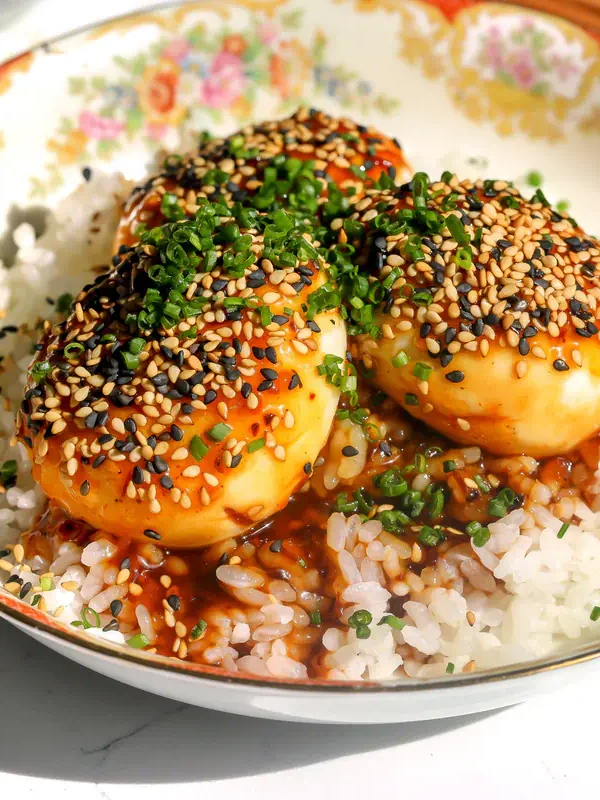 Three tiger skin eggs with sauce, sesame seeds, and chives over white rice in a floral bowl, with chopsticks resting across the rim.