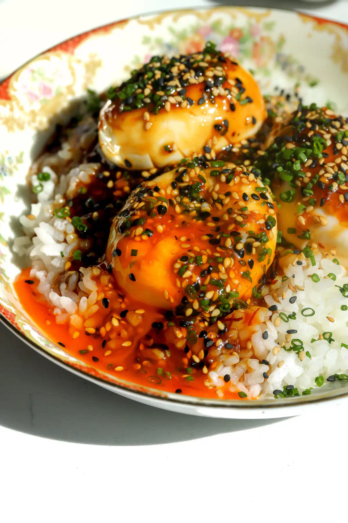 A tiger skin egg broken open, with orange yolk running into the sauce and white rice, topped with sesame seeds and chives.