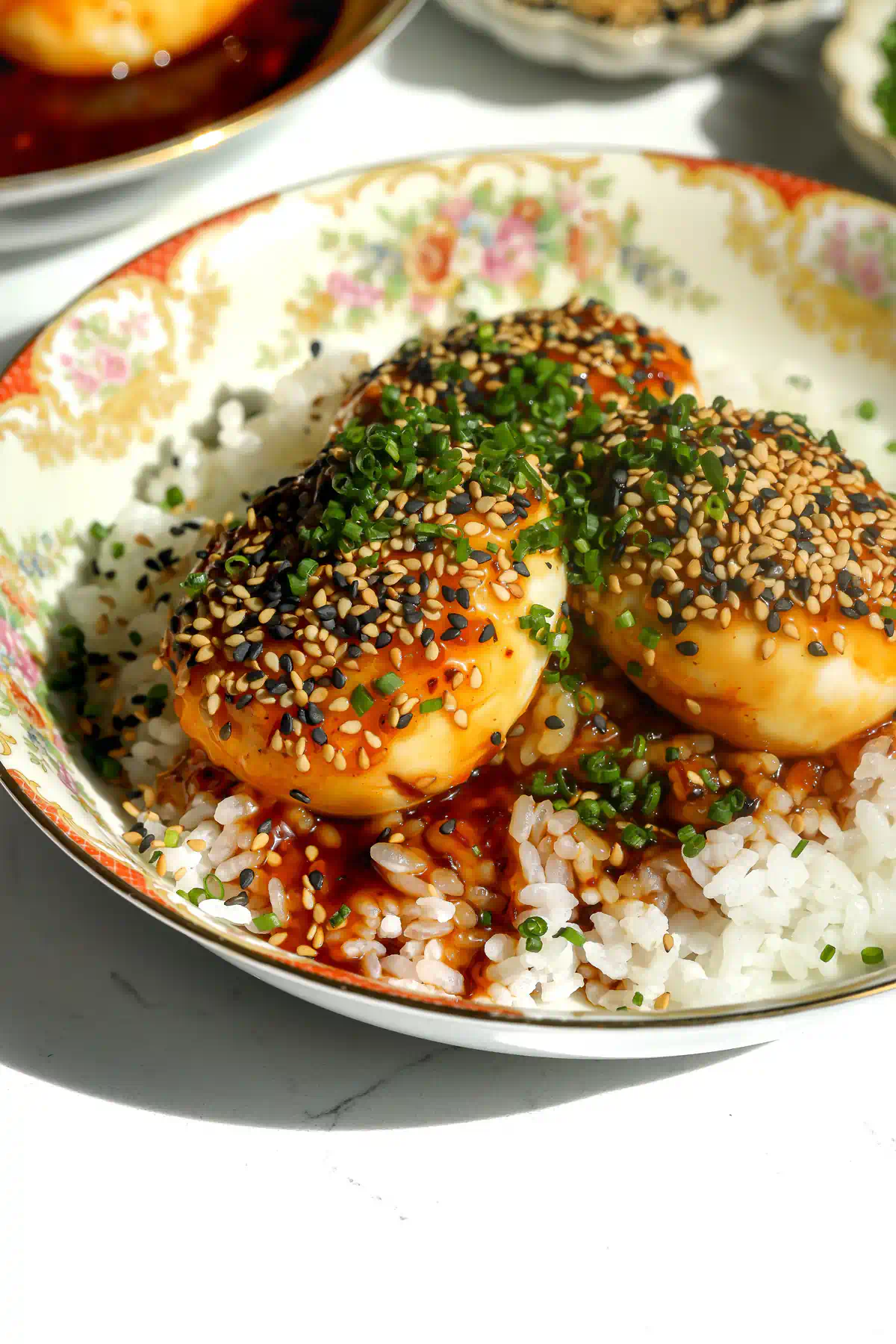 Close-up of tiger skin eggs over white rice, coated in sauce and topped with black and white sesame seeds and chopped chives.